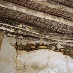 Wooden beams support the reeds and other roofing materials. One can see the stonework and coatings.