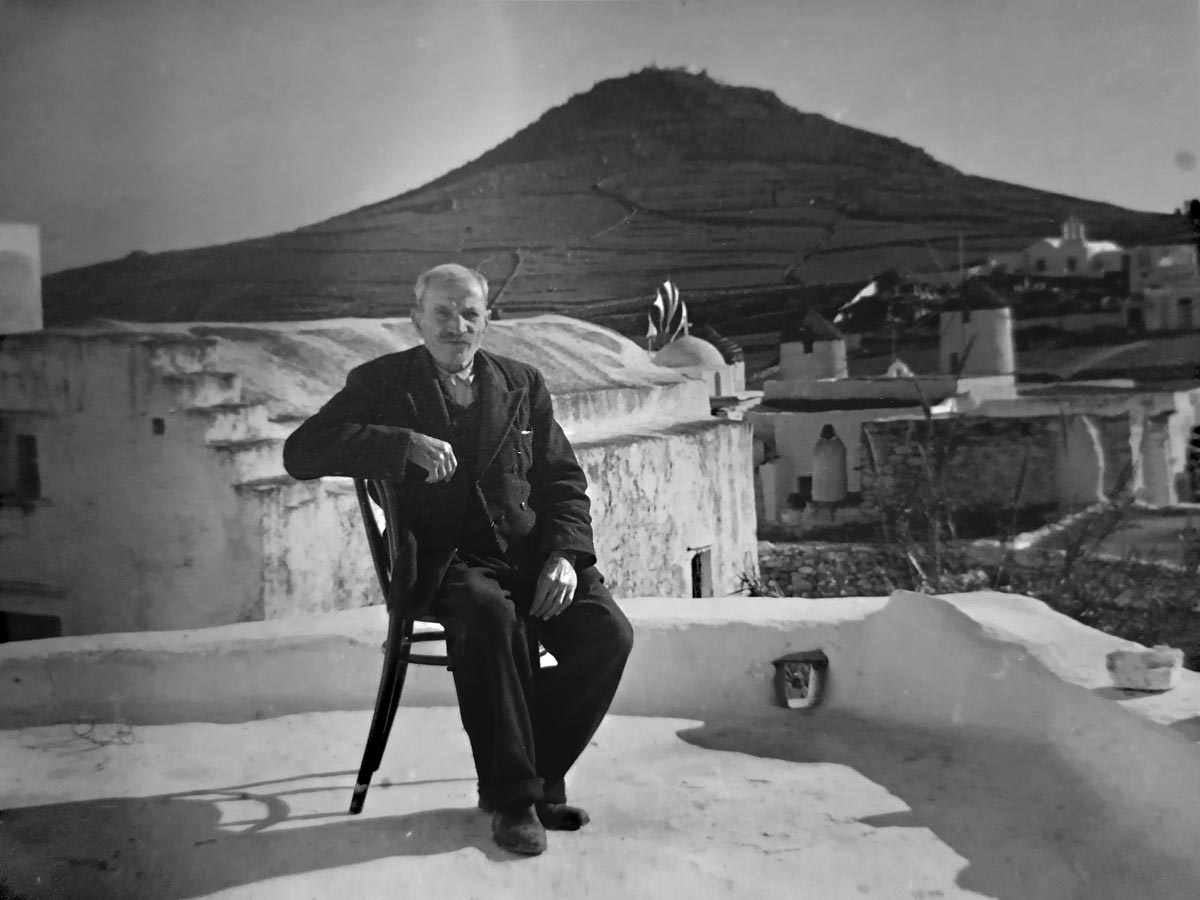Stamatis Malamatenios at the veranda of the house with the church of Saint Antonios in the background.